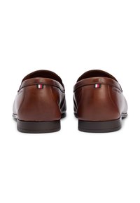 Καφέ δερμάτινα loafers με λείο φινίρισμα, σχεδιασμό χωρίς κορδόνια, στρογγυλερή μύτη και μινιμαλιστικές ραφές. Διαθέτουν μικρή διακοσμητική σημαία.