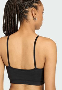 Čierny skrátený top s tenkými ramienkami, vyrobený z mäkkého materiálu, s ryhovanou textúrou a priliehavým strihom. Minimalistický štýl.