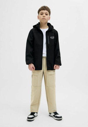 Svart zip-up jacka med huva, framfickor, lager på en vit t-shirt. Beige cargobyxor med sidfickor, svarta och vita sneakers.