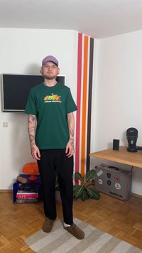 Πράσινο βαμβακερό μπλουζάκι με πολύχρωμο γραφικό φρούτων και κείμενο "ADIDAS ORIGINALS", συνδυασμένο με μαύρο παντελόνι και καφέ παπούτσια τύπου slip-on.