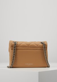 Sac à main matelassé beige avec chaîne en argent et détail de logo. Matériau en simili cuir doux, forme rectangulaire compacte, texture lisse.