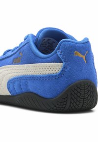 Blå mockasnör sko med vit läderrand, texturerad svart gummisula och guld Puma-logotyp som accent. Har en vadderad krage för komfort.