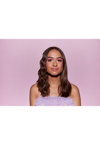 Fioletowa, teksturowana bluzka z miękkiego, puszystego materiału; modelka ma falowane włosy i intensywny różowy cień do powiek na tle w pastelowym różu.