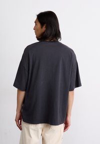 T-shirt surdimensionné gris foncé à manches courtes, en coton, de coupe décontractée et à col rond, vu de l'arrière.