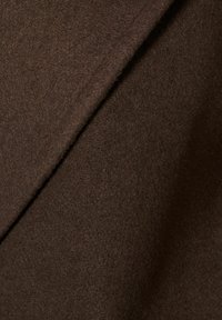 Dettaglio ravvicinato di un tessuto di lana marrone scuro con una consistenza morbida e pelosa e una cucitura diagonale.