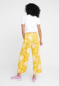 Breda byxor med blommönster i gult och ett lätt mönster, med elastisk midja, tillsammans med en vit t-shirt med korta ärmar och rosa sneakers.