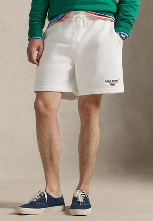 Biele fleecové šortky so sťahovacou šnúrkou v páse. Na nich je čierne logo Polo Sport s červenými a modrými akcentmi. Nosia sa s námorníckymi plátenými topánkami.