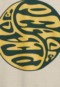 La tela beige presenta un gran gráfico circular en amarillo y verde oscuro, que muestra un diseño abstracto con formas fluidas e interconectadas.