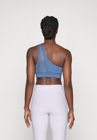 Blauwe sportbeha met een enkele brede band en een meshpaneel, gecombineerd met lichtgrijze high-waisted legging, gladde textuur en aansluitend ontwerp.