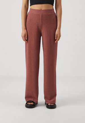 Ribbade stickade vida byxor i en dammig rosafärg, med hög midja och textilmaterial, tillsammans med svarta sandaler som glids på.