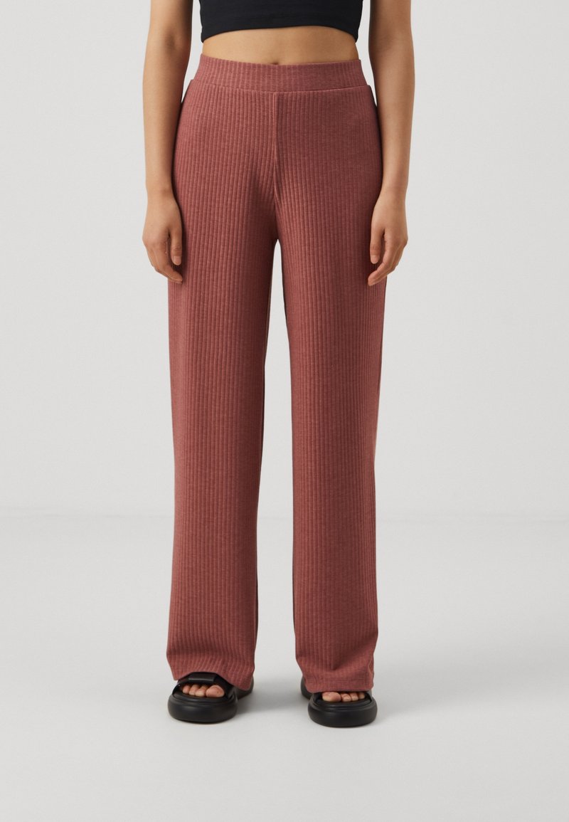 Pantalons larges en tricot côtelé de couleur rose poussiéreux, dotés d'une taille haute et d'un tissu texturé, associés à des sandales noires à enfiler.