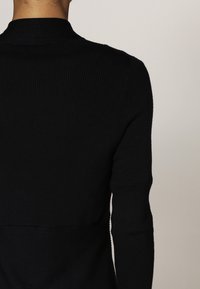 Svart ribbad stickad tröja med en åtsittande design, som har en hög krage och långa ärmar, och visar en slät textur och rena linjer.