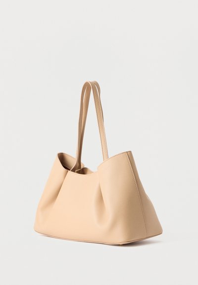 Μπεζ δερμάτινη τσάντα χειρός με δύο λεπτές λουριά ώμου, μαλακή δομή και μινιμαλιστικό σχεδιασμό, τοποθετημένη σε απλό λευκό φόντο.