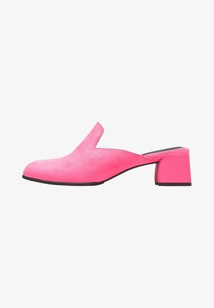 Mules de ante rosa con un recorte en forma de V y un tacón bajo y cuadrado. Textura suave con una suela negra en contraste.