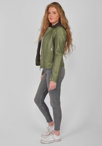 Grön läderjacka med dragkedja framtill och sidofickor. Bärs över en grå hoodie, tillsammans med gråa skinny jeans och vita sneakers.