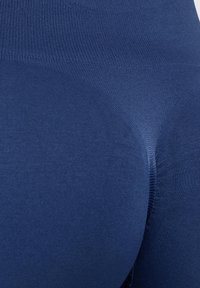 Granatowe legginsy wykonane z rozciągliwego materiału, z gładką fakturą, wysokim pasem i dopasowanym krojem, który podkreśla sylwetkę. Dodatkowe akcenty to wzmocnione szwy.