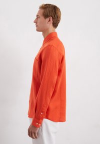 Long-sleeve, bright orange shirt in lightweight fabric with a buttoned cuff, featuring a chest pocket and a classic collar design.