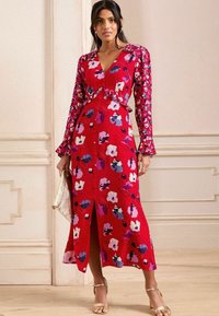 Vestido floral rojo con escote en V y mangas largas. Presenta una cintura con volantes y un dobladillo dividido. Adornado con flores moradas, rosas y blancas.