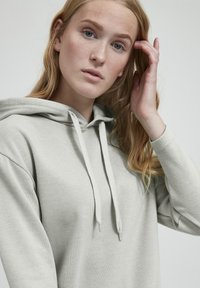 Hellgrauer Hoodie mit strukturiertem Finish, featuring eine Fronttasche, verstellbare Kordeln und einem lässigen Schnitt. Weicher Stoff.
