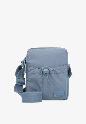 Light blue fabric crossbody bag with a top drawstring closure, adjustable strap, and a small logo patch on the front.