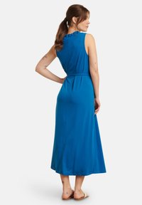Maxi dress in bright blue fabric, sleeveless with a high neckline and back ruffle detail. Features a tied waist and flowy silhouette.