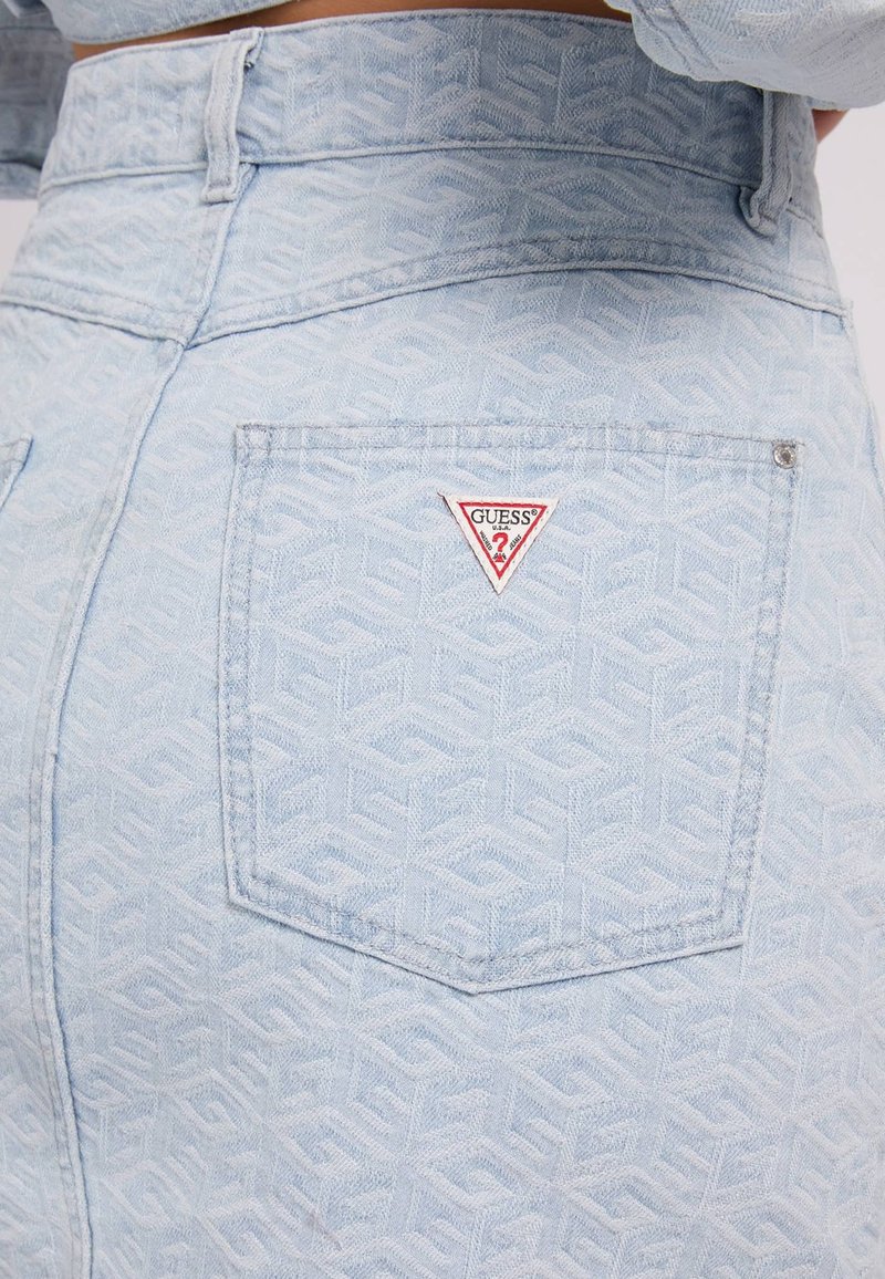 Falda de denim azul claro con un patrón texturizado, con un logo triangular rojo y blanco de "GUESS" en el bolsillo trasero.