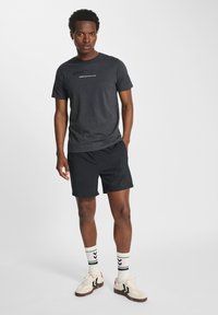 Svart sportströja med tryck "SPORTS DEPT", i kombination med svarta shorts, vita strumpor med svarta ränder och beige sneakers. Enkel och atletisk design.