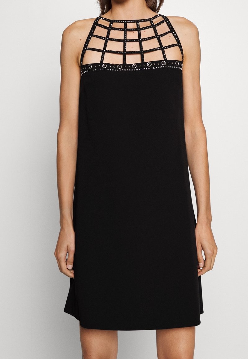 Robe noire sans manches avec un décolleté à motif quadrillé orné de petits clous argentés et de décorations circulaires le long du bord supérieur.
