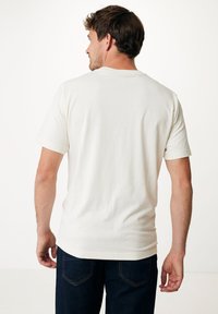 Krémové bavlněné tričko s krátkými rukávy, kulatým výstřihem a hladkou texturou. Nosené s tmavými džíny, ukazující pohodlný střih.