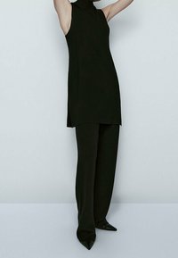Black sleeveless tunic with a high neckline, paired with wide-legged black trousers and pointed-toe black heels, minimalist design.