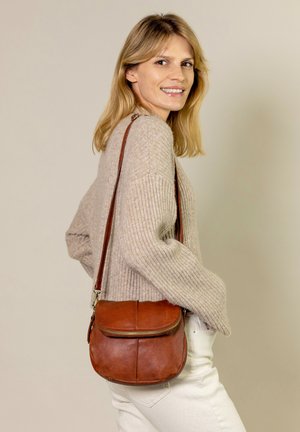 Borsa a tracolla in pelle marrone con tasca anteriore con zip, texture liscia, forma arrotondata e tracolla regolabile, abbinata a un maglione beige lavorato a maglia.