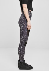 Sorte leggings med et himmelsk mønster av stjerner og måner, med teksturert stoff og ensfargede svarte detaljer på knærne.