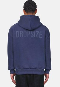 Navy blue hoodie with a large "DROPSIZE" print on the back. Features a drawstring hood, ribbed cuffs, and a relaxed fit. Soft fabric texture.