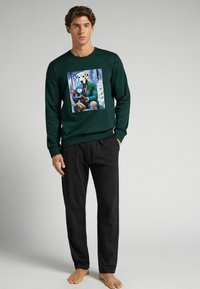 Groene sweatshirt met lange mouwen met een bedrukte afbeelding van een man in een pak met een hondenhoofd, gecombineerd met zwarte losse broek.