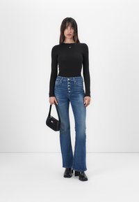 Top nero a maniche lunghe con design aderente, jeans blu a vita alta svasati con chiusura a bottone, borsa nera e stivali con tacco.