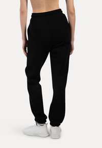 Sorte sweatpants lavet af blød stof, med elastisk talje og cuff, samt sidelommer. Båret med hvide sneakers.