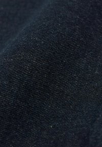 Denim tkanina, tamnoplave boje, sa suptilnom teksturom. Krupni plan prikazuje uzorak tkanja i blagu dlačicu, što ukazuje na strukturirani materijal.