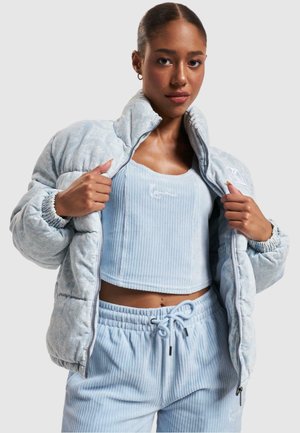 Light blue puffer jacket with a patterned fabric, zip closure, and elastic cuffs, layered over a matching ribbed crop top and sweatpants.