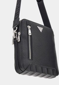 Schwarze, strukturierte Leder-Umhängetasche mit Reißverschlüssen in Silberoptik, einem Logo-Emblem und einem gepolsterten Boden. Verfügt über einen verstellbaren Tragegurt.