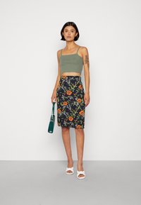 Top verde cropped, saia pérola preta com padrão floral em tons de laranja e verde, sandálias brancas e uma bolsa verde.