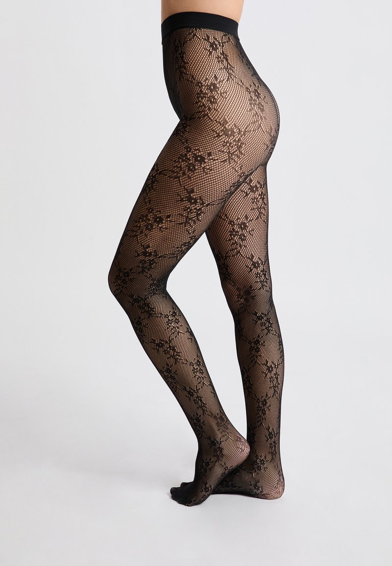 Medias de red negras con un patrón de encaje floral, una cinturilla alta y una textura transparente, diseñadas para cubrir completamente las piernas.