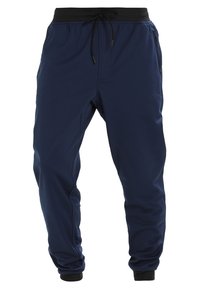 Mörkblå joggingbyxor med svart elastisk midjeband och dragsko, zip-fickor på sidorna och muddade anklar.