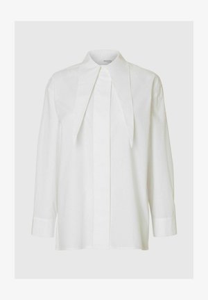 Balta garām piedurknēm blūze ar uzsvērti izteiktu punktētu apkakli un apslēptu pogu rindu, fona gaismā.