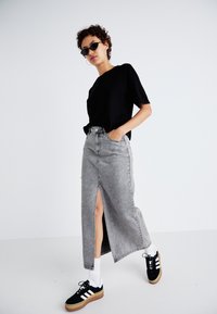 Grå denim maxikjol med en framtill ficking, ihop med en svart t-shirt och svarta sneakers med vita ränder och en gummisula. Tillbehören inkluderar små solglasögon.