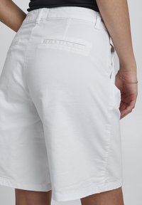 Hvide bomulds shorts med en afslappet pasform, der har baglommer og en glat overflade. Kanten er lige og slutter lige over knæet.