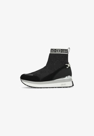Bottine de sport noire avec un upper en tricot texturé, des accents en daim, une bande logo au col et un détail métallique le long de la semelle.