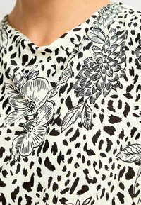 Tessuto bianco con un motivo a stampa floreale e animale in nero, con fiori e foglie mescolati tra forme astratte.