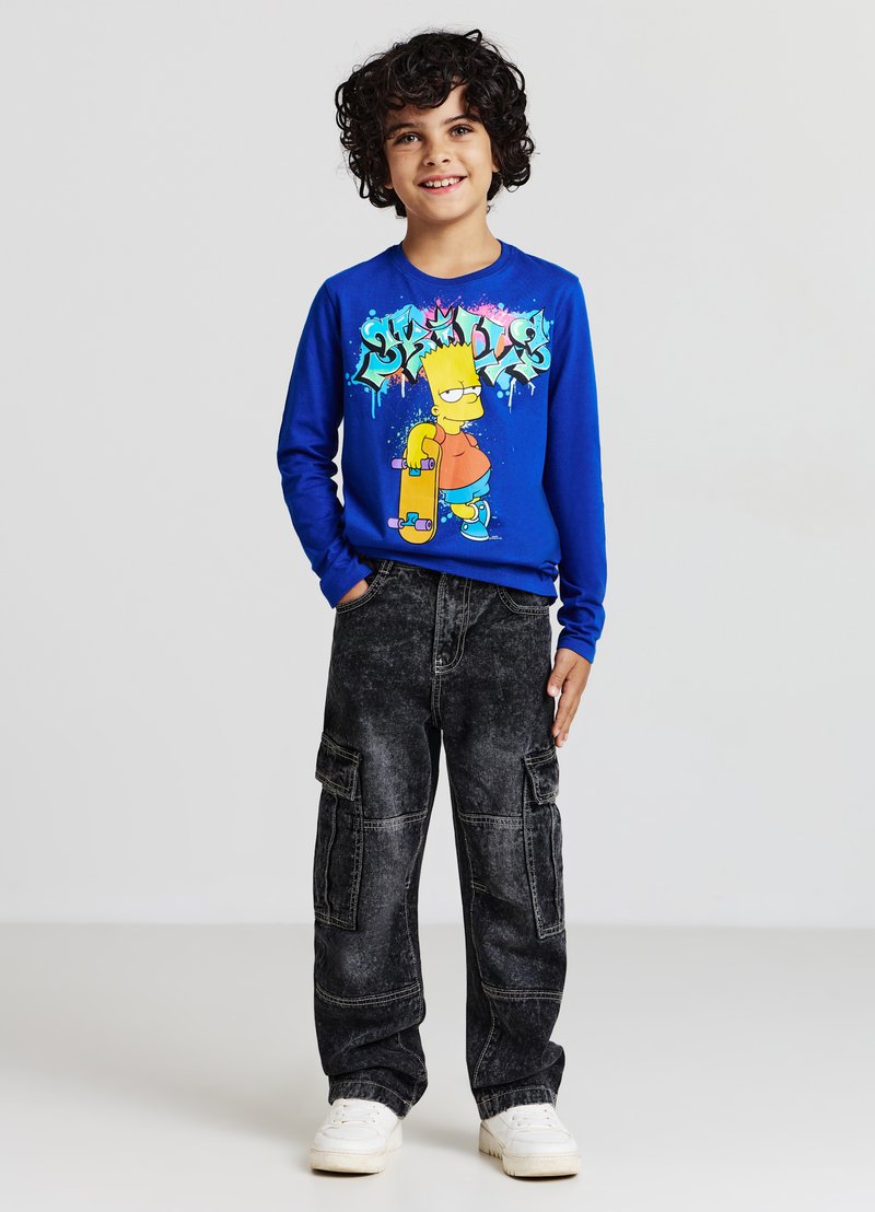 Maglietta a maniche lunghe blu con una grafica colorata di un personaggio con uno skate, abbinata a pantaloni cargo neri e sneaker bianche.