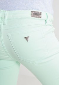 Jean skinny vert menthe avec une texture lisse. Accent logo en métal sur la poche arrière. Détails de couture distincts partout.