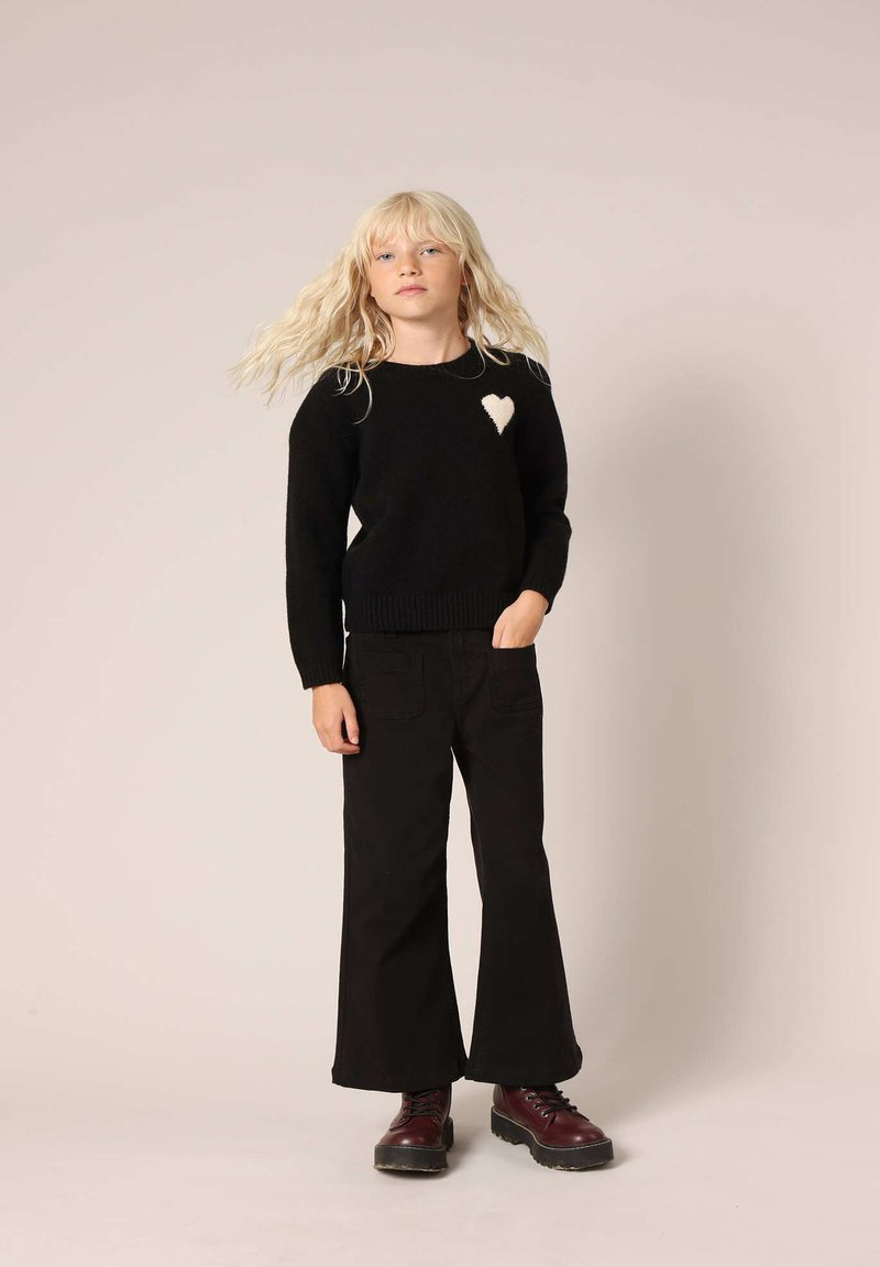 Zwarte trui met een crèmekleurig hartdetail, geribde halslijn en onderrand. Gecombineerd met zwarte wijde broek en bordeauxrode veterschoenen.